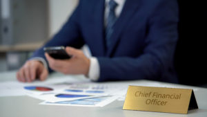 Chief Financial Officer at a desk reviewing financial documents and charts, holding a smartphone.