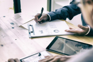 Two professionals collaborating at a wooden table, analyzing charts and graphs on a clipboard and tablet, focusing on data-driven insights